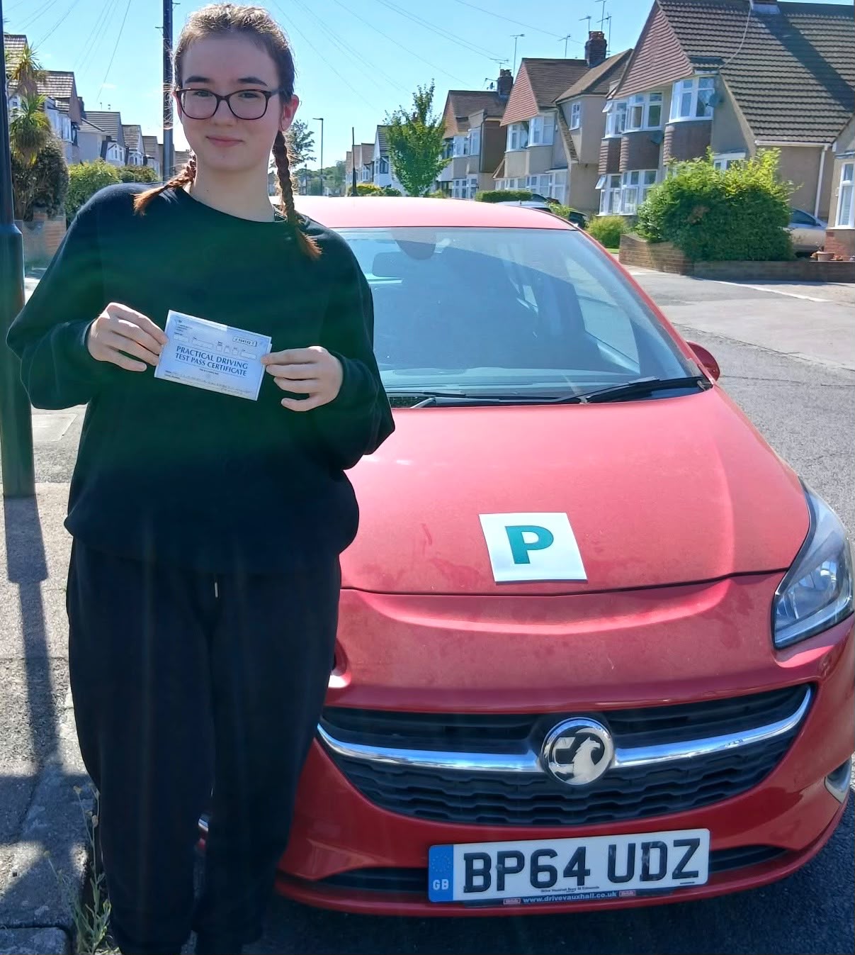 Amelia standing beside her new red car holding her practical driving test pass certificate, after passing with Bexleyheath Driving School
