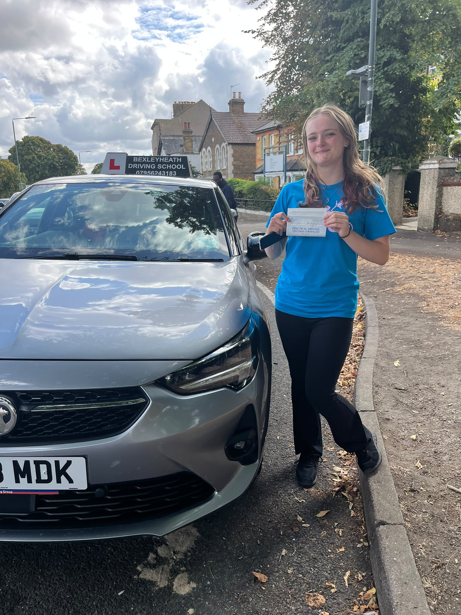 Jess standing beside the Bexleyheath Driving School car holding her practical driving test pass certificate after passing first time at Belvedere Driving Test Centre